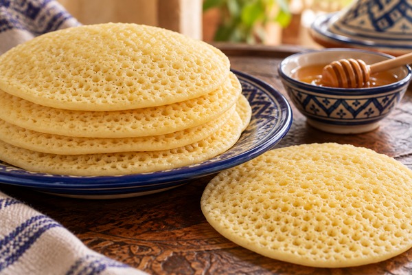 Baghrirs moelleux à la surface alvéolée servis sur une assiette avec du miel